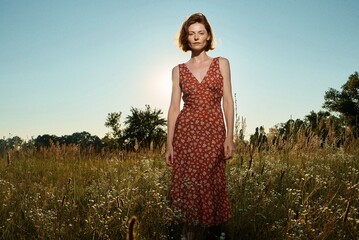 A woman in a floral dress stands in a sunlit field at golden hour