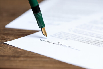 Signing notary document with fountain pen at wooden table, closeup
