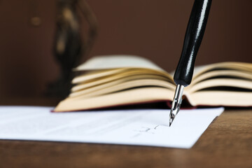 Signing notary document with fountain pen at wooden table against brown background, closeup