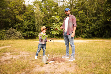 Father and his son planting tree into soil outdoors