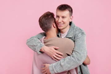 Fototapeta premium Two happy friends hugging on pink background