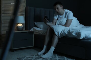 Frustrated man with alarm clock suffering from insomnia on bed indoors