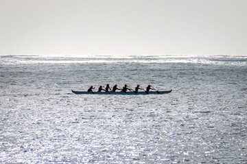 Outrigger canoe paddling along the coast of the island of Oahu, Hawaii, USA in a single hulled boat against the light