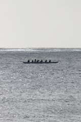 Outrigger canoe paddling along the coast of the island of Oahu, Hawaii, USA in a single hulled boat against the light