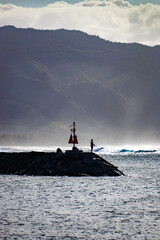 Man fishing while standing on breakwater at Haleiwa harbor fishing point, Oahu, Hawaii, USA against the light