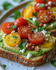 Avocado toast topped with red and yellow cherry tomatoes, crumbled feta cheese, chopped walnuts and fresh herbs on rustic bread, macro food photography.