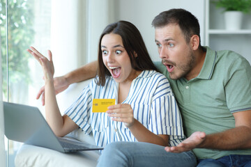 Amazed couple paying online with laptop and card