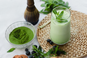 Glass of iced green matcha latte with mint garnish placed on a woven placemat, styled with...