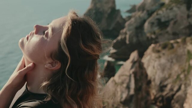 A woman with closed eyes dances passionately by the ocean cliffside, embracing the serene and powerful surroundings.