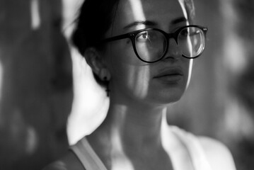 A striking black and white portrait of a woman wearing glasses, thoughtfully looking away.