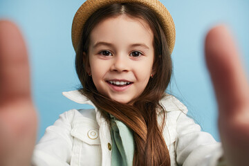 Cute girl in trendy hat and clothes taking selfie against blue background