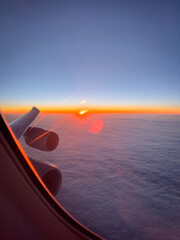Bright sunset above the clouds seen through an aircraft window with visible lens flare and window reflections