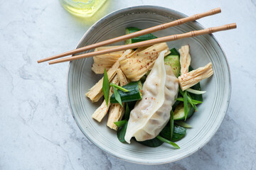 Tofu skin, smashed cucumber salad and pork dumpling in a grey bowl, horizontal shot on a white...