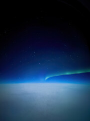 Aurora borealis northern lights seen from an airplane window at night, glowing above a blanket of...