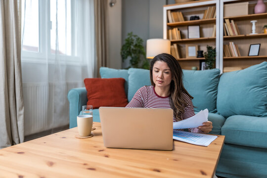 Young strong independent freelance businesswoman, small startup business company owner, sitting at home on floor, working on laptop computer, looking data, invoices and statistic. Independence concept