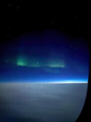 Aurora borealis northern lights seen from an airplane window at night, glowing above a blanket of clouds against a blue sky with stars