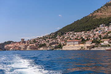 View of a Mediterranean coastal town and hillside from the sea. Boat wake leads the eye toward the...