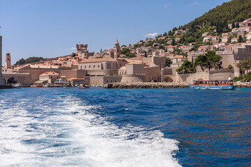 Approaching an old walled city by boat, with splashing water in the foreground. Historic...