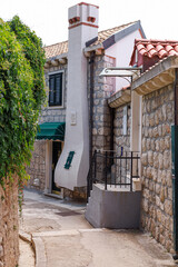 Fototapeta premium Picturesque corner of a stone alley with a unique chimney and green awning on a traditional house. Peaceful Mediterranean atmosphere.