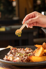 Chef adding argentinian chimichurri sauce to grilled steak with potatoes