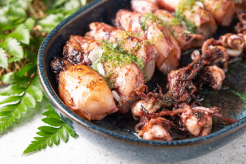 Grilled squids with green sauce and parsley lying on dark plate