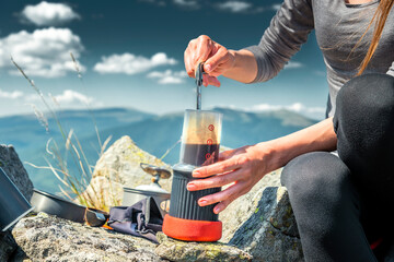 Woman brewing coffee with AeroPress on mountain summit. Outdoor adventure, travel gear