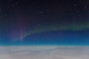 Aurora borealis northern lights seen from an airplane window at night, glowing above a blanket of clouds against a blue sky with stars