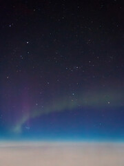 Aurora borealis northern lights seen from an airplane window at night, glowing above a blanket of clouds against a blue sky with stars