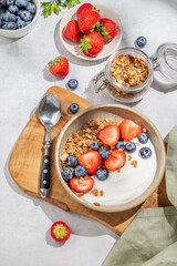 Natural yogurt with granola, blueberry and strawberry in a bowl on a wooden board on a light background
