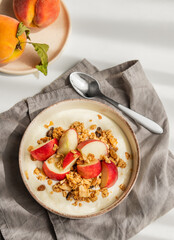 Natural greek yogurt with granola or muesli and peach in a bowl on a napkin on a  white background