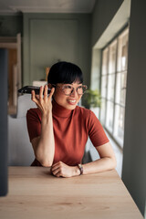 Smiling Woman Talking on Speakerphone at Her Desk in a Well-Lit Office
