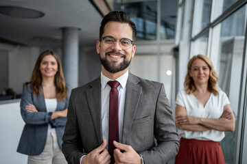 Smiling businessman adjusting suit with coworkers in background in office