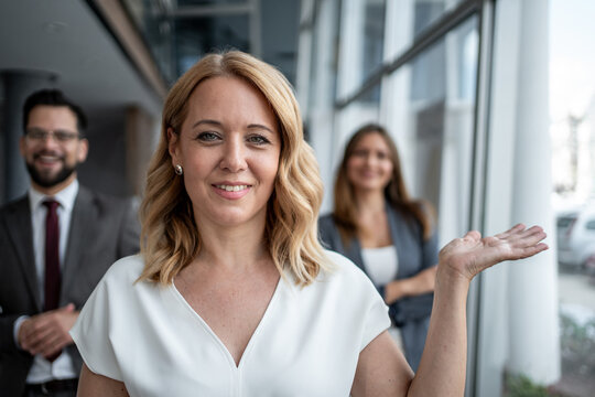Businesswoman showing something with hand gesture to colleagues in office hallway