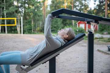 Young woman training on outdoor gym machine in park on a sunny day