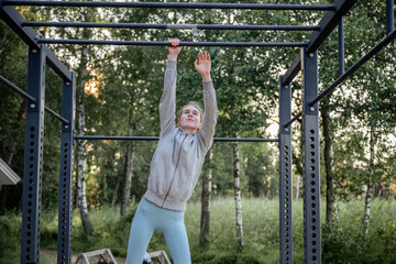 Fototapeta premium Young woman hanging on pull-up bar at outdoor gym in park