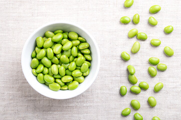Edamame beans in a white bowl on linen. Shelled young, immature soybeans, Glycine max, of green color, often eaten as snack, steamed or boiled. Popular side dish and appetizer in East-Asian cuisine.