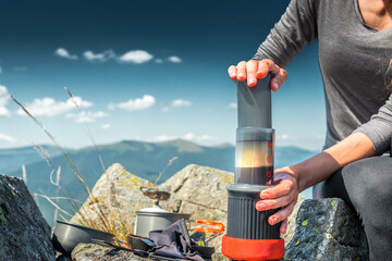 Woman brewing coffee with AeroPress on mountain summit. Outdoor adventure, travel gear