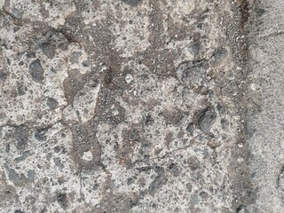 Rough concrete surface filled with fractures, natural dirt buildup, and scattered stones.