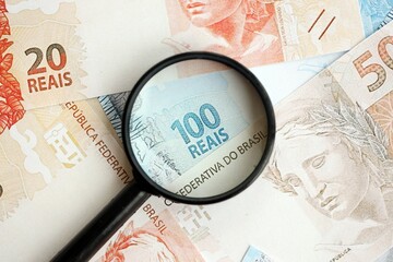 Brazilian reais banknotes and magnifying glass. The current Brazil real money bills and loupe