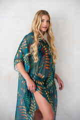 Fototapeta premium Young blonde female wearing boho-inspired pareo dress with exotic patterns, minimal background fashion photo