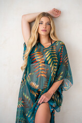 Young blonde female wearing boho-inspired pareo dress with exotic patterns, minimal background...