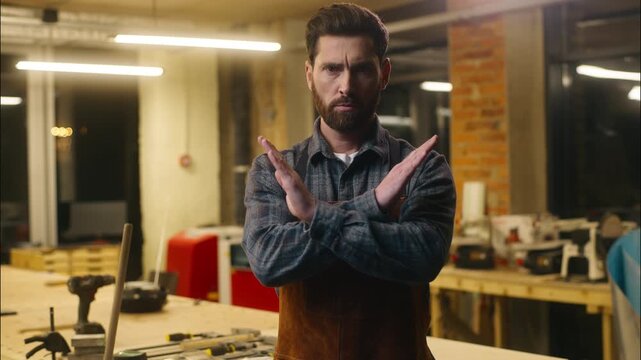 Serious Caucasian wood master man show prohibition gesture in workshop craftsman forbid builder joiner rejection guy demonstrating cross with hands male repairman ban no symbol artist decline refusing