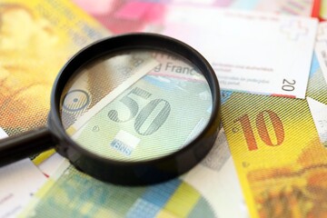 Swiss franc banknotes and magnifying glass. The current francs money bills with loupe lies on table