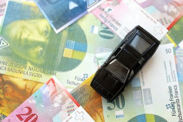 Swiss franc banknotes and toy car. The current francs money bills and black car lies on table