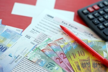 Swiss franc banknotes and tax form with pen. The current francs money bills lies on tax return form
