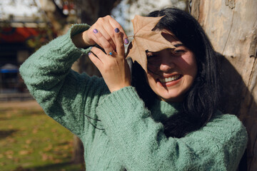 Happy young woman protects herself from the sun by covering her face with a leaf