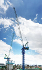 Aerial view of two tower cranes the important construction machinery working on a construction site with image of building on summer blue sky background.
