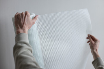 Male hands holding a roll of white plaster mesh for preparatory and painting works.