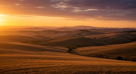 Rolling hills bathed in the warm glow of the setting sun, with a cloudy sky above, creating a scenic landscape.