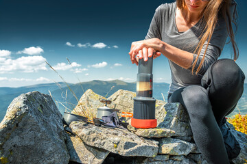 Woman brewing coffee with AeroPress on mountain summit. Outdoor adventure, travel gear
